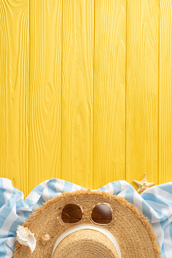Summer dreamscape: vertical top view straw hat, sunglasses, beach blanket, shell, and starfishes on a yellow wooden background