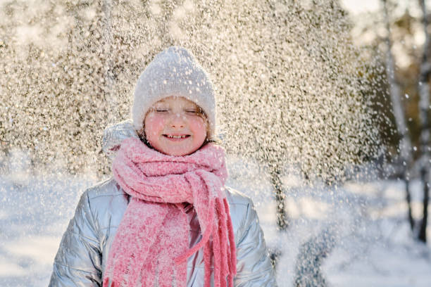 Cute cheerful girl in warm winterwear enjoying snowfall while standing in natural environment on winter weekend