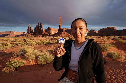 Navajo Woman in Her Forties in Front of Totem Pole Rock in Monument Valley Tribal Park Utah Holding an I Voted Sticker Signifying that She Just Voted in an American Election