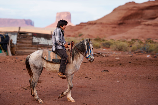 Handsome Young Fourteen Year Old Navajo Boy Wearing Cowboy Hat Riding His Horse Bareback on a Ranch in Monument Valley Arizona