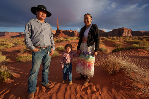 Traditional Navajo Married Couple with Two Year Old Boy Viewing Totem Pole Rock in Monument Valley Tribal Park at Dusk with Cloudscape and Patterns in the Sand