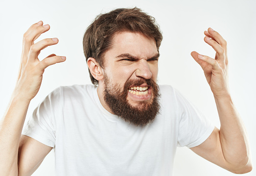 Emotional man gesticulates with his hands on a light background and a thick beard irritability. High quality photo