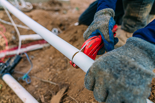 Irrigation Construction Woker using a PVC pipe cutter to cut a polypropylene sprinkler line in new construction outdoors