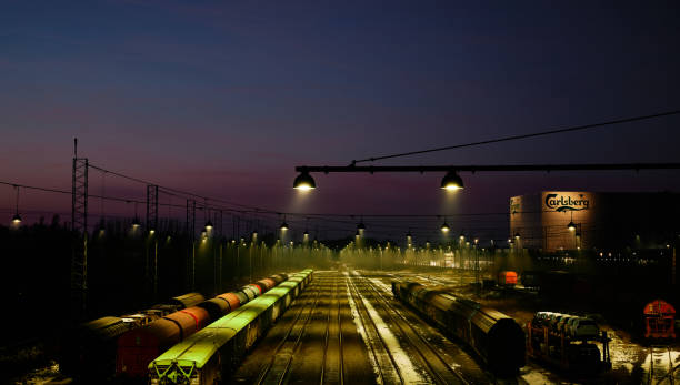 Fredericia, Denmark. January 12, 2024. High angle view of lights illuminating over trains parked on railway tracks against blue sky at night