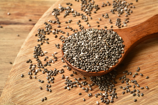 Close up of chia seeds in a spoon on wooden table. Chia seeds contain fibre and omega-3 fatty acids, protein, many essential minerals and antioxidants. Healthy eating concept.