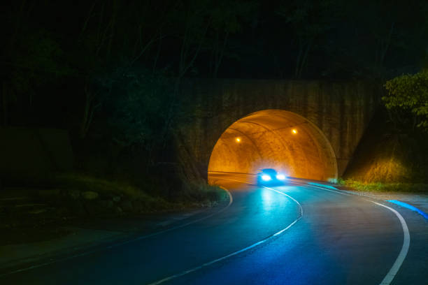 istock Highway in the evening. The car pulls out from under the bridge. A car with its headlights on leaves the tunnel. Night travel by car. Country road in the dark. Road with a tunnel. 2149867605