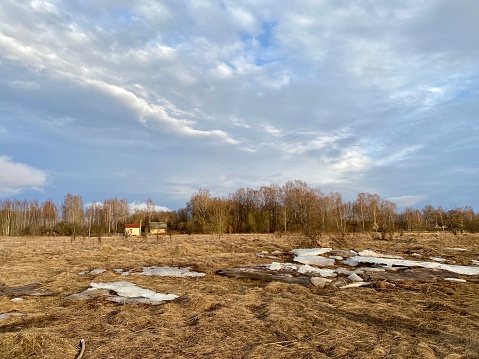 Spring village landscape: cloudy sky, dry grass and large white ice floes on the field.