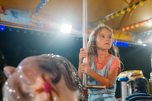 Caucasian little girl ride a vintage horse carousel in the evening at an amusement park on on her summer holiday