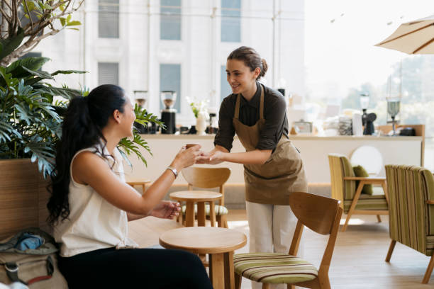 Friendly waitress serving cup of coffee to customer in cafe
