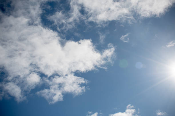 A picturesque scene of billowy clouds adorning the azure canvas of the sky, creating a tranquil ambiance in the springtime. This shot has the sun and some solar spots