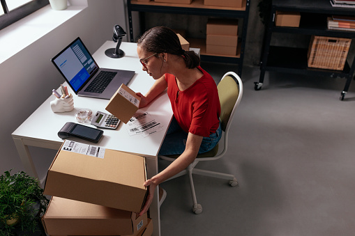 An efficient female entrepreneur organizing and examining multiple parcels on her desk in a modern office setup