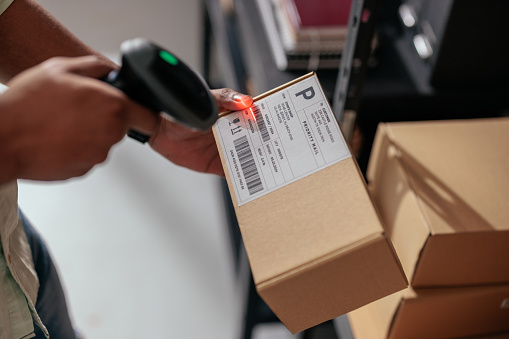 Closeup of a man scanning barcode on package in a warehouse setting to manage inventory and order processing