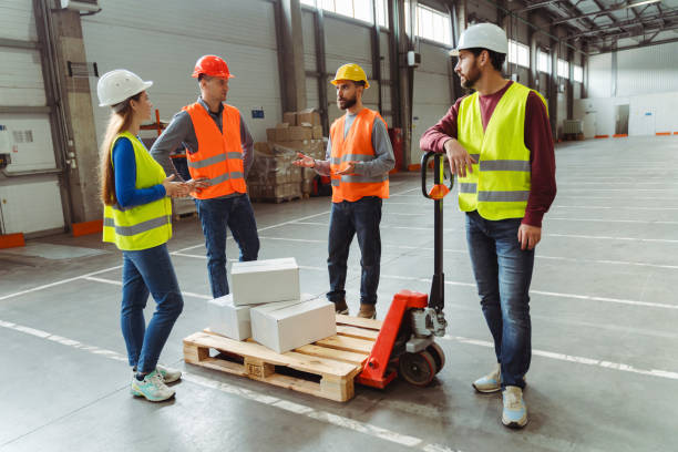 istock Group of successful managers, workers wearing safety helmet and vest loading boxes on pallet truck 2149876954