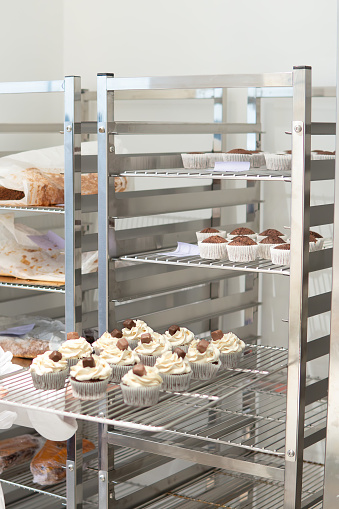 cupcakes and mini cakes on trays are placed on industrial bakery trolleys. Spain Europe