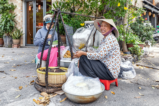 Ho Chi Minh, Vietnam - March 12, 2024: Vietnamese woman in a traditional conical hat, sells Vietnamese food on the street in the center of Ho Chi Minh