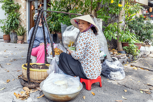 Ho Chi Minh, Vietnam - March 12, 2024: Vietnamese woman in a traditional conical hat, sells Vietnamese food on the street in the center of Ho Chi Minh