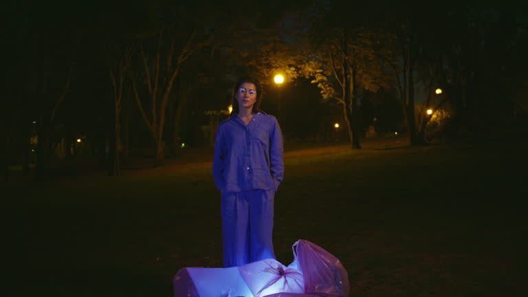 Stylish woman participating park cleanup at night illuminated by streetlights.