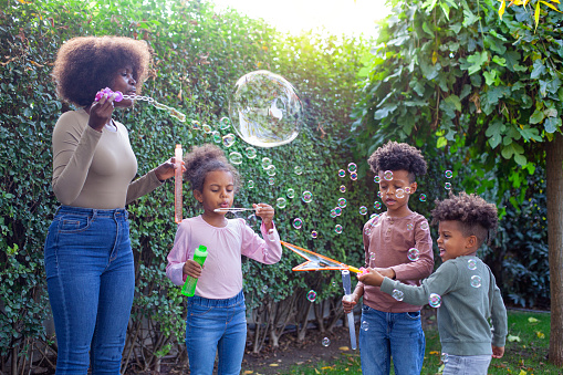 Happy family playing soap bubbles on a picnic for bonding time together on grass in summer