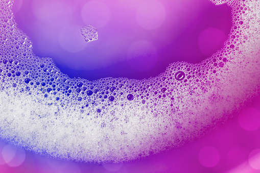 Close-up of soap suds with water on a purple background. Beautiful bokeh light, space for copy.