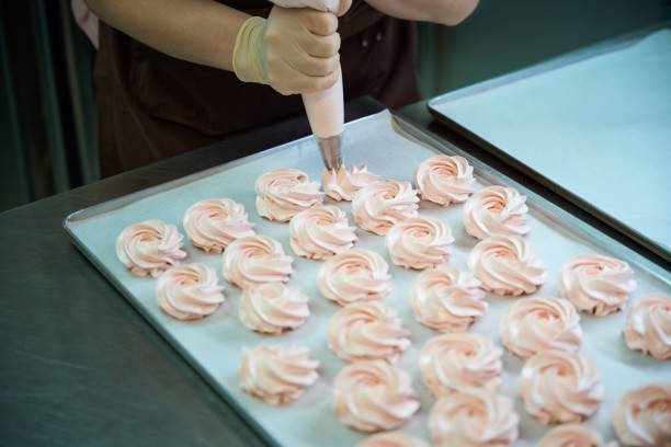 Woman cook pushing on the pastry bag with sweet fruit mixture inside, making like flowers circles on the baking paper, cooking delicious and tasty sweet dessert