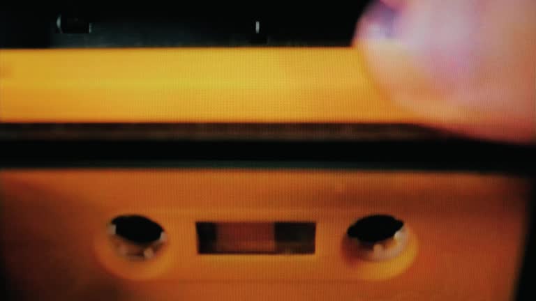 Real TV capture: putting a yellow cassette tape (obsolete audio storage technology) into a deck and playing it. Broken item getting stuck. Front close-up shot.