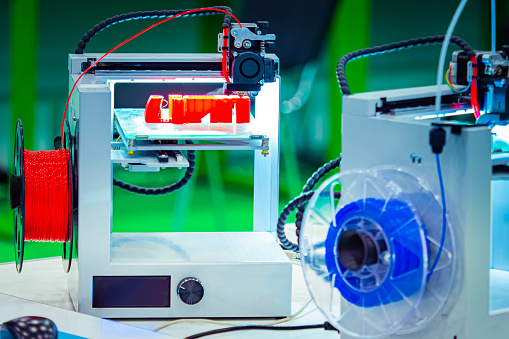 3D printers close up. Print objects from blue and red materials. Method of layer-by-layer model construction. The printer prints a three-dimensional object. Modern technology.