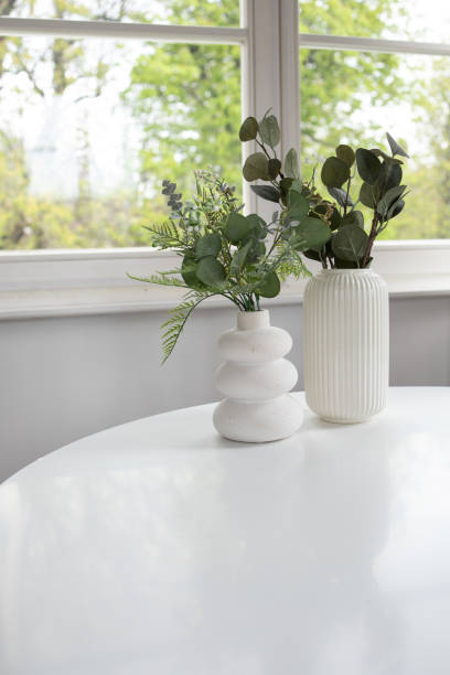 istock Background of two white vases with artificial greenery on white table and window at the back 2149892103
