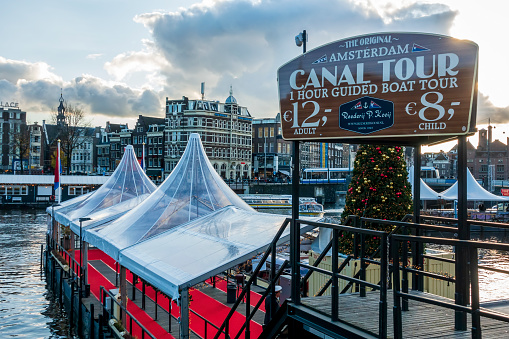 Amsterdam, Netherlands - Dec 1, 2019: Sign to the Original Amsterdam Canal Boat Tour for tourists. Wooden jetty leading to awaiting boat from street level.