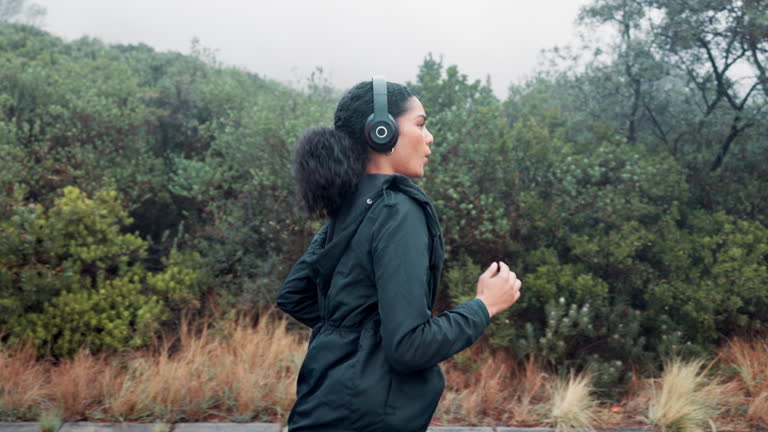 Woman, headphones and running on mountain for healthy workout with music listening, podcast or exercise. Female person, fitness and nature wellbeing with pop playlist for training, morning or misty