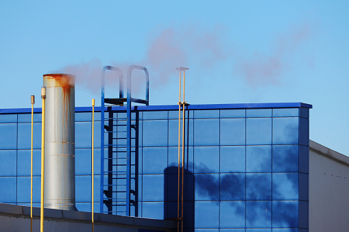 Chimneys of a heating system on the facade of a residential building, Europe. Chimney with smoke, stairs, wall, building facade in blue.