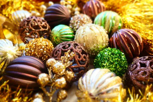 New Year's Christmas balls, tinsel and decorations close up. A lot of decoration of golden, brown, yellow, green. Striped Christmas balls. Festive beautiful colorful background. Home holidays design