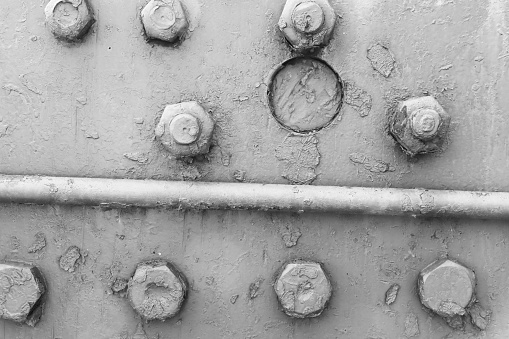 Background of an abandoned metal wall with bolts and tube, with damaged gray paint.