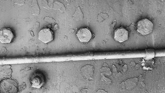 Background of an abandoned metal surface of metal armor with bolts, with damaged gray paint,
and technical metal pipe.
