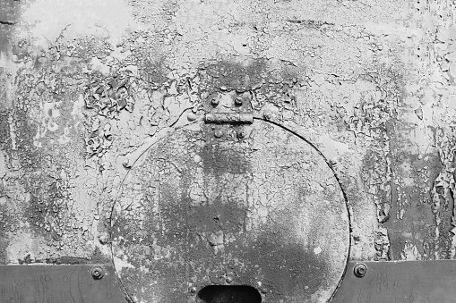 The side of an old technical vehicle with a hatch, covered with damaged gray paint.