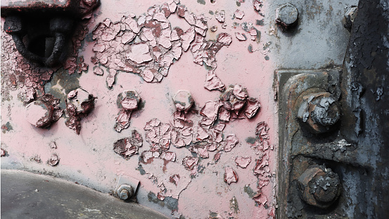 A fragment of the side of an abandoned steam locomotive with bolts, with damaged peeling red paint.