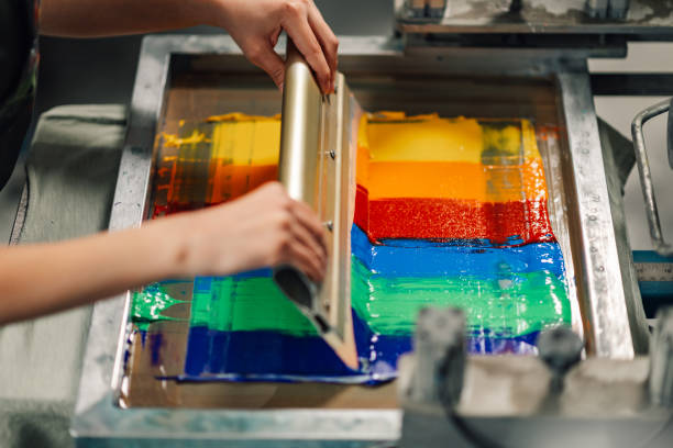 istock Close up of graphic worker's hands screen printing with squeegee. 2149896634