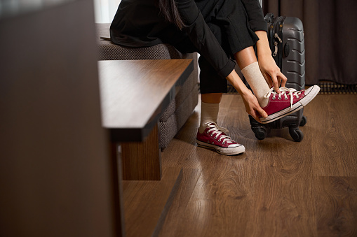 Business lady taking off her shoes while sitting on the sofa in the hotel room. Travel, lifestyle, people concept