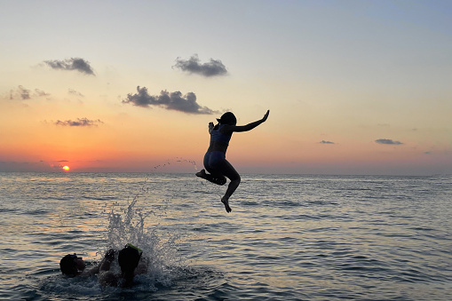 Child jumps in the sea against sunset sky with sun and clouds. Happy family having fun on sea beach