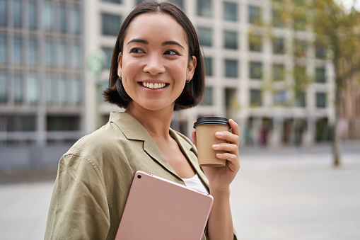 Retrato de una chica asiática con una tableta, bebe café en la calle, camina por el centro de la ciudad photo
