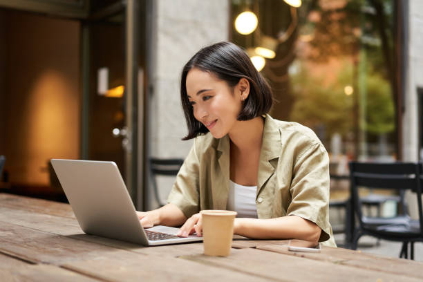 istock Young asian woman, digital nomad working remotely from a cafe, drinking coffee and using laptop, smiling 2149903806