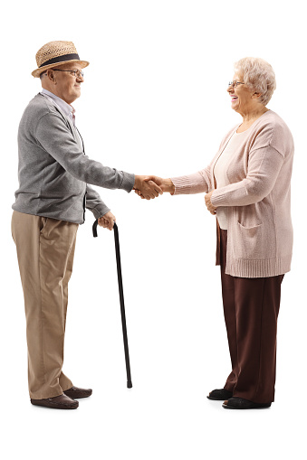 Full length profile shot of an elderly man and an elderly woman shaking hands isolated on white background