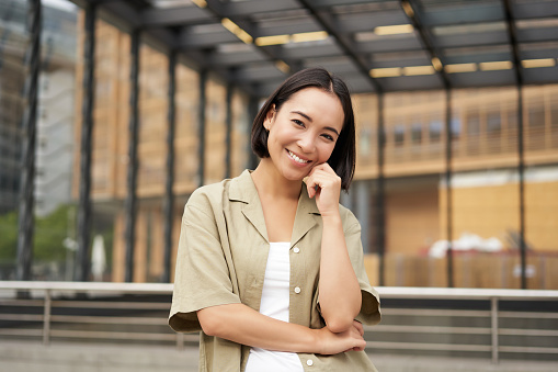 Portrait of beautiful young woman in casual clothes, smiling, posing outdoors on an empty street near glass building photo