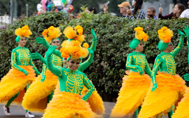 29th Oct, 2022, Mexico City, Mexico State, Mexico. Female dancers in green tops and orange frilly skirts at a huge annual Day of the Dead parade that takes place in Mexico City at the end of every October. The Day of the Dead is celebrated all over Mexico at the end of October with paredes, fiestas and families observing and revering their deceased  loved ones at their graves.