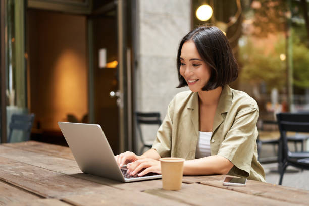 istock Young asian woman, digital nomad working remotely from a cafe, drinking coffee and using laptop, smiling 2149907614