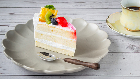 Bake vanilla cake with fruit topping on a plate with hot black coffee. On the background of a white wooden board