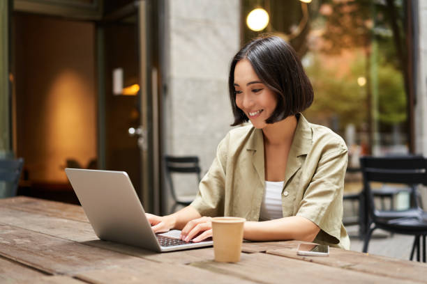istock Young asian woman, digital nomad working remotely from a cafe, drinking coffee and using laptop, smiling 2149910836