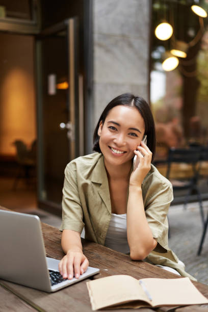 istock Happy girl calling on mobile phone, talking on smartphone and working with laptop, doing homework, studying outdoors from cafe 2149910912