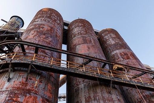 The iconic rusty Bethlehem Steelstacks with towers and pipes in Pennsylvania. The massive metal structures, characterized by a patina of rust and intricate pipework, rise against the blue sky. Low angle view