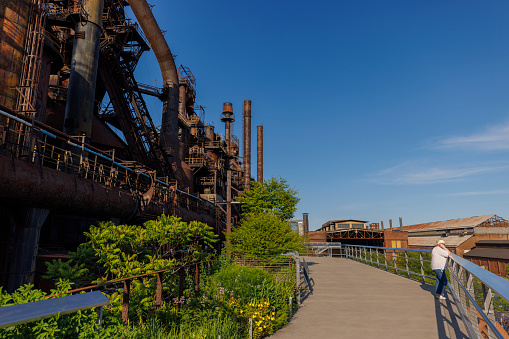 Plump Caucasian woman explores the abandoned Steelstacks plant in Bethlehem, Pennsylvania. Walking along the pathway, she admires the rusty structures that once formed the backbone of the local steel industry