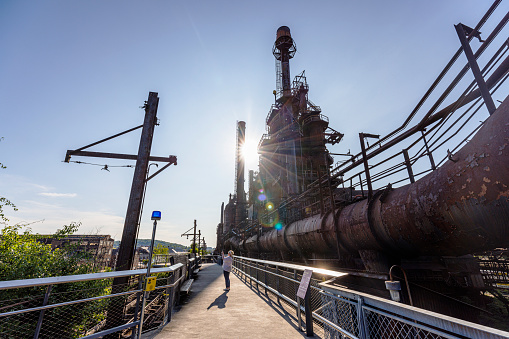 Body-positive Caucasian woman tourist, explores Steelstacks —  the iconic abandoned steel plant in Bethlehem, Pennsylvania at sunset. The industrial setting provides juxtaposition between industrial decay and natural light